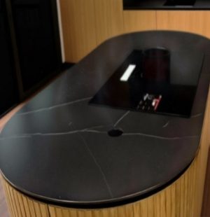 Овальная керамическая столешница Dekton черного мрамора с белыми прожилками, интегрированной варочной панелью. Современный минималистичный дизайн кухонного острова.
